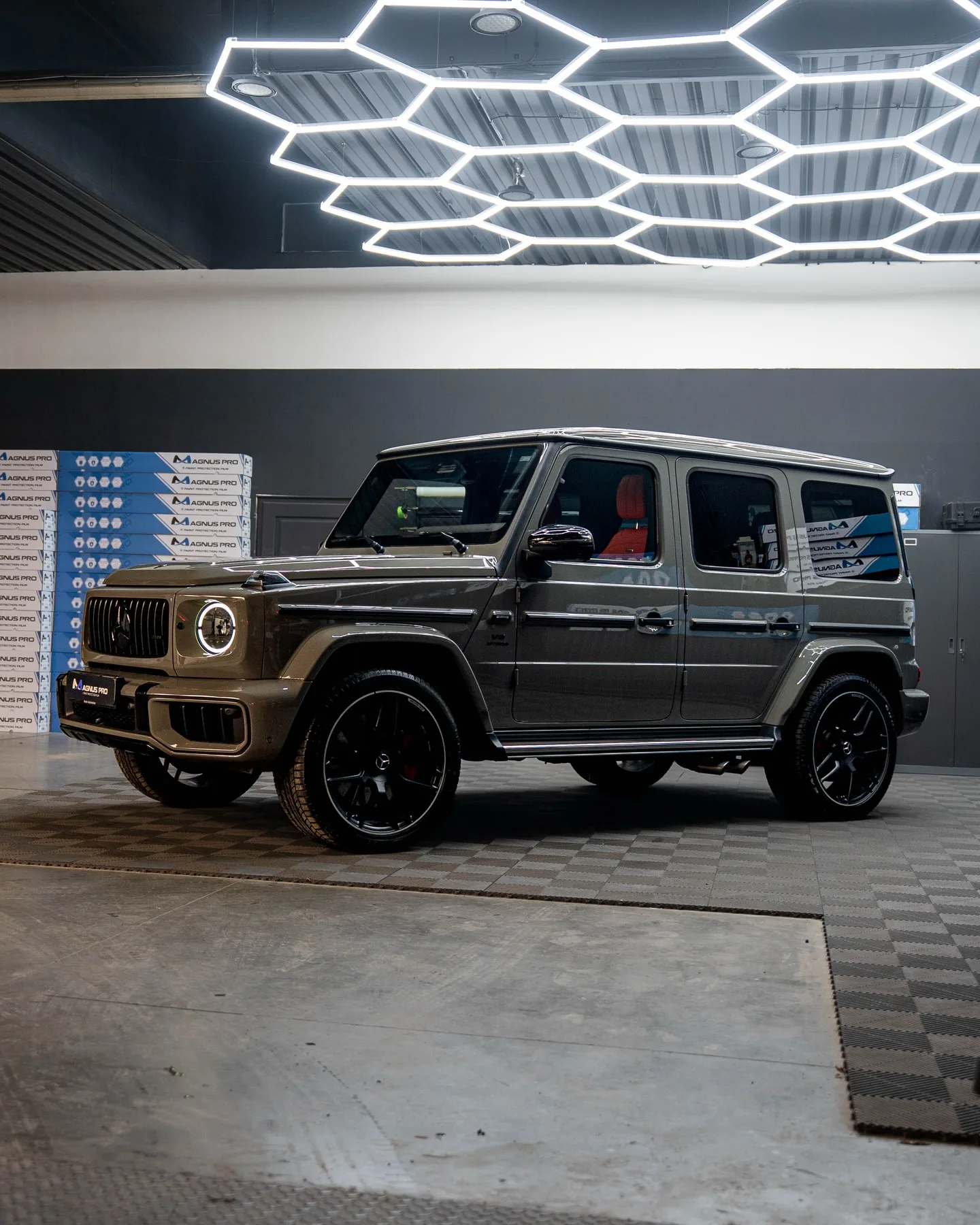 Sivý Mercedes-Benz G63 v aplikačnom centre Magnus Pro v Košiciach, s regálmi ochrannej fólie v pozadí