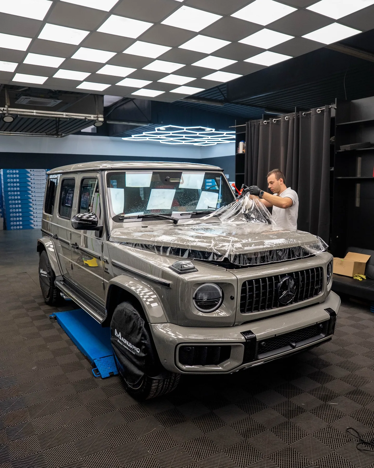 Aplikátor kladie ochrannú fóliu na kapotu sivého Mercedesu-Benz G63