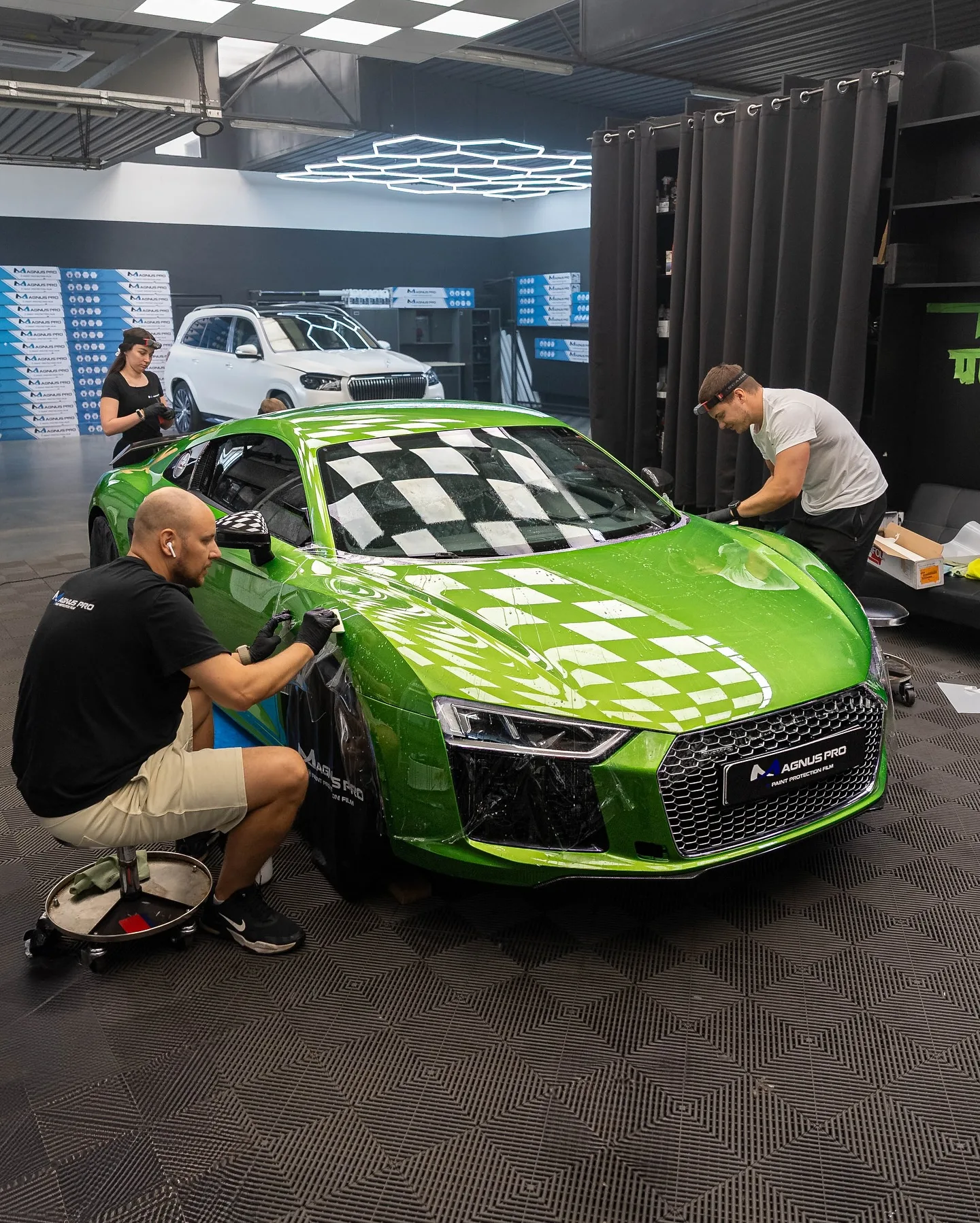 Dvaja aplikátori kladú ochrannú fóliu Magnus Pro na zelené Audi R8 v aplikačnom centre