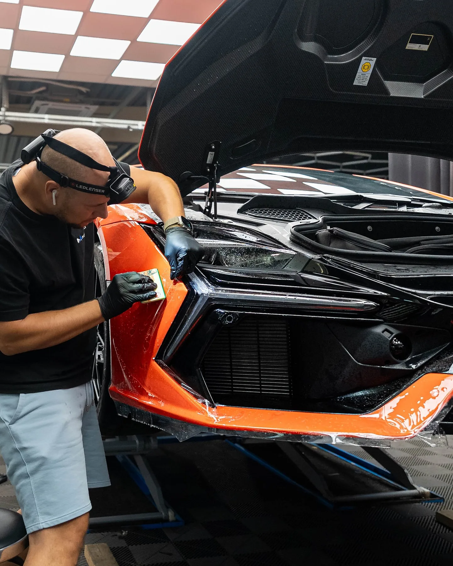 Aplikátor nanáša ochrannú fóliu Magnus Pro na predný nárazník oranžového Lamborghini Revuelto